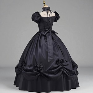 May include: A black ball gown with a high collar and short, puffed sleeves. The dress features a fitted bodice with a lace-up back and a full skirt adorned with bows. A large bow accents the back waist.