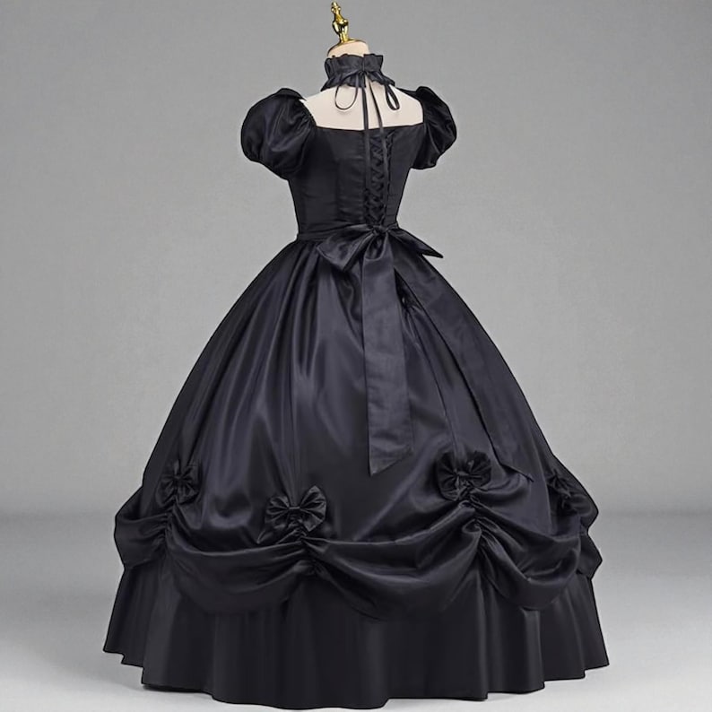 May include: A black ball gown with a high collar and short, puffed sleeves. The dress features a fitted bodice with a lace-up back and a full skirt adorned with bows. A large bow accents the back waist.