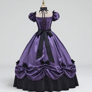 May include: A purple and black Victorian-style gown. The bodice is a deep purple with a lace-up back and short, puffed sleeves. A black bow adorns the waist, and the skirt is a full, layered design with black accents. The dress is displayed on a mannequin.