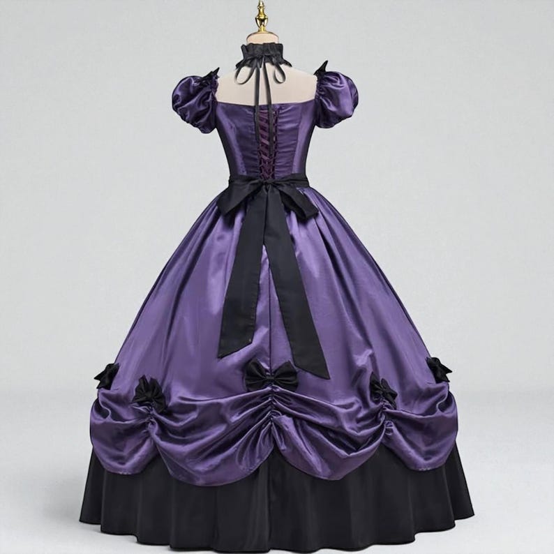 May include: A purple and black Victorian-style gown. The bodice is a deep purple with a lace-up back and short, puffed sleeves. A black bow adorns the waist, and the skirt is a full, layered design with black accents. The dress is displayed on a mannequin.