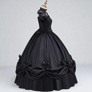 May include: A black ball gown with a high collar and short sleeves. The dress features a fitted bodice, a full skirt, and decorative bows. The gown is displayed on a mannequin against a plain background.