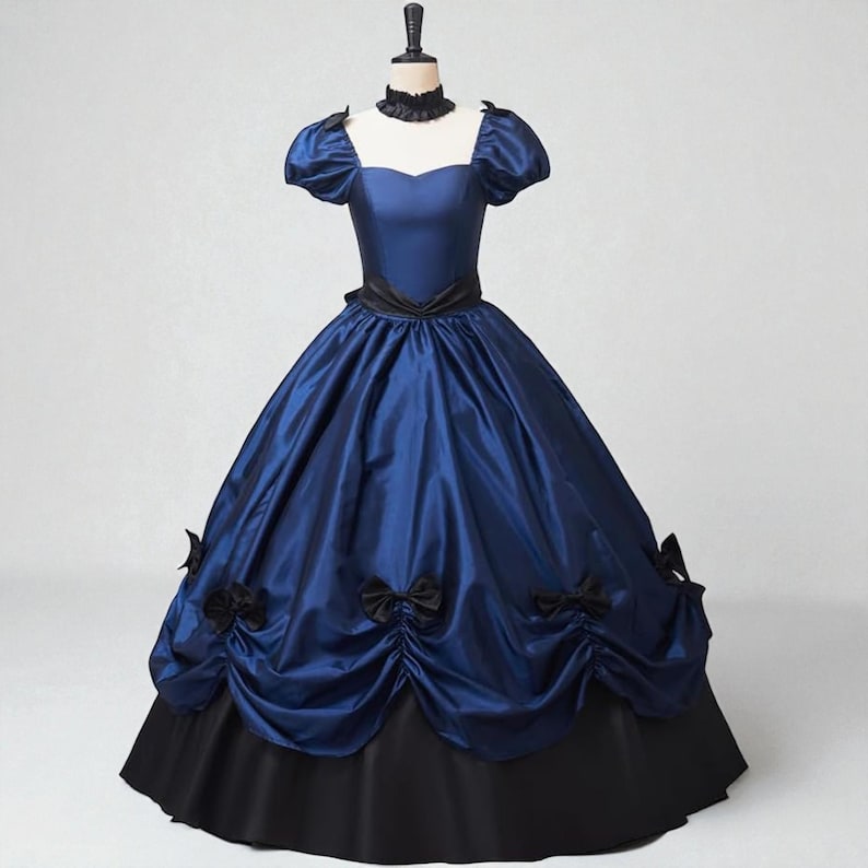 May include: A blue and black ball gown with a square neckline and short, puffed sleeves. The dress features a black ribbon at the waist and black bows on the skirt. The skirt is a full, layered design.