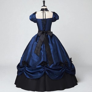 May include: A navy blue ball gown with a black skirt and accents. The dress features a square neckline, short puffed sleeves, and a black bow at the waist. Black rosettes adorn the skirt.