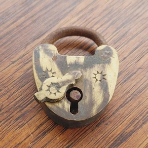 Peut inclure: Un cadenas de style vintage avec un trou de serrure et une anse arquée rouillée. Le cadenas a une finition crème et marron avec des motifs en forme d'éclat d'étoile. La clé est insérée. Le cadenas est sur une surface en bois.