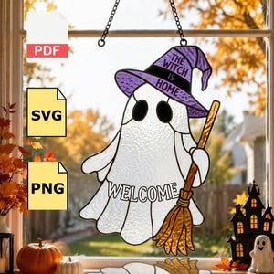 Puede incluir: Un atrapasoles de vidrieras con forma de fantasma que lleva un sombrero de bruja morado con el texto THE WITCH IS HOME. El fantasma sostiene una escoba marrón y tiene la palabra WELCOME impresa en su cuerpo. Cuelga de una cadena de metal negro.