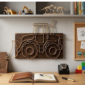 Puede incluir: Decoración mural con contorno de tractor dorado, montada sobre una tabla de madera rectangular. El tractor es un diseño de alambre. El fondo incluye una estantería con juguetes de construcción y esqueletos de dinosaurios, y un escritorio con un cuaderno y bolígrafos.