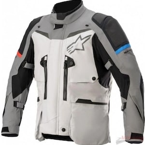 以下が含まれることがあります： Alpinestarsのロゴが入った、グレー、白、黒のバイク用ジャケット。ジャケットには複数のポケット、ジッパー、調節可能なストラップが付いています。袖には赤と青のアクセントが見えます。保護とスタイルを考慮して設計されています。