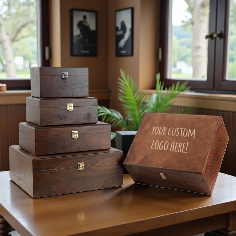 May include: A set of dark brown wooden boxes of different sizes, with metal clasps, displayed on a wooden table. One box is inscribed with the text "YOUR CUSTOM LOGO HERE!". The boxes are suitable for storage.