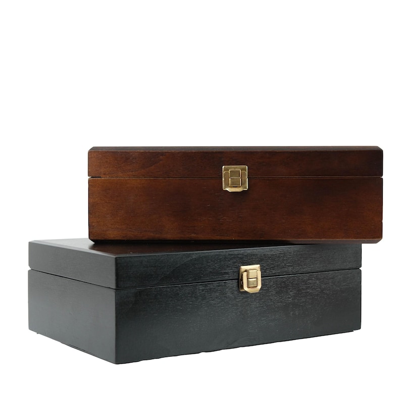 May include: Two wooden boxes, one dark brown and one black, stacked. Each box has a rectangular shape with a brass-coloured clasp. The boxes are likely for storage or display, with a classic design.