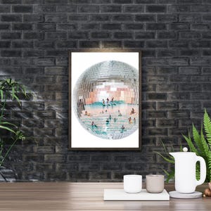 May include: A rectangular wall art print featuring a large, spherical disco ball. The mirrored surface of the disco ball reflects a bright, sunny scene of people swimming and surfing in turquoise ocean water under a clear, light blue sky.