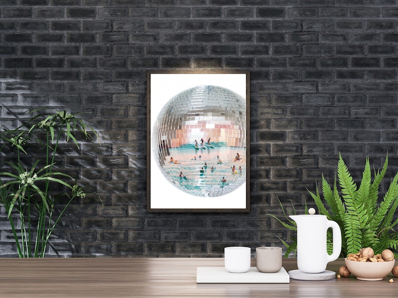 May include: A rectangular wall art print featuring a large, spherical disco ball. The mirrored surface of the disco ball reflects a bright, sunny scene of people swimming and surfing in turquoise ocean water under a clear, light blue sky.