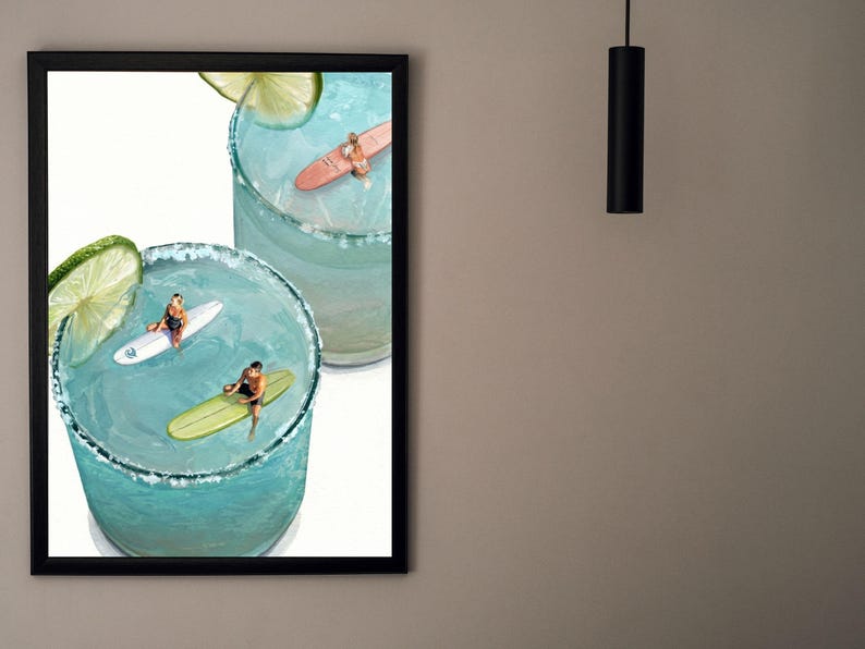 May include: A framed wall art print featuring two light blue cocktails in glasses with salt rims and lime slices. Inside the drinks, three miniature figures are surfing on small surfboards, with one person on a white board, one on a green board, and one on a pink board.