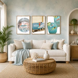 May include: Three framed wall art prints displayed above a sofa. The left print shows a disco ball filled with swimmers. The center print depicts a person surfing on a vinyl record. The right print features two glasses of blue cocktails with surfers.