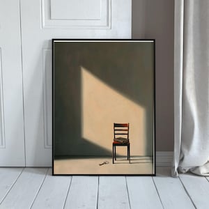 Könnte beinhalten: Gerahmter Kunstdruck mit einer minimalistischen Innenszene. Ein Holzstuhl mit einem Buch steht in einem sonnigen Bereich, mit einem Schlüssel auf dem Boden. Das Kunstwerk ist schwarz gerahmt, vor einer neutralen Wand und weißem Boden.