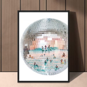 May include: A framed wall art print featuring a large, spherical disco ball with a mirrored surface. The interior of the sphere displays a surreal scene of people surfing and swimming in turquoise ocean waves under a bright, clear sky.