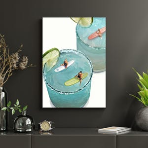 May include: A vertical wall art print featuring two glasses of blue liquid with salt-rimmed edges and lime slices. Inside the glasses, miniature figures are depicted surfing on small white, yellow, and pink surfboards atop the blue liquid surface.