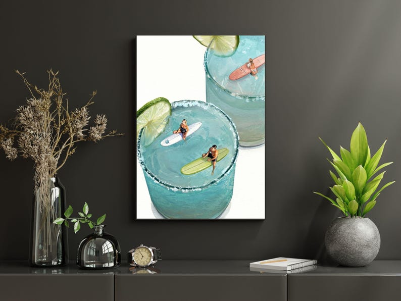 May include: A vertical wall art print featuring two glasses of blue liquid with salt-rimmed edges and lime slices. Inside the glasses, miniature figures are depicted surfing on small white, yellow, and pink surfboards atop the blue liquid surface.