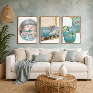 May include: Three framed wall art prints displayed above a white sofa. The left print shows surfers inside a disco ball. The center print features a person surfing on a record player. The right print depicts surfers in a cocktail glass.