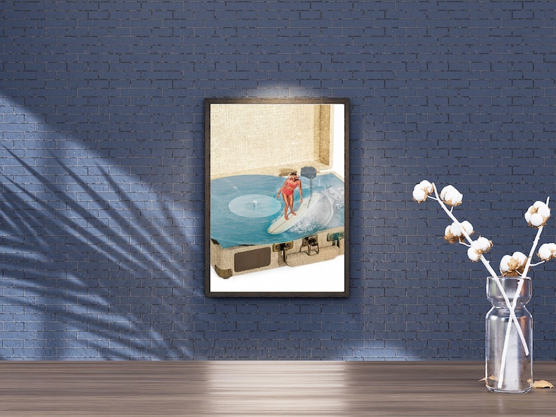 May include: A framed wall art print featuring a surreal collage of a vintage suitcase open to reveal a blue vinyl record spinning. A person in a red swimsuit is surfing on a white surfboard atop the record, with a wave crashing on the side.