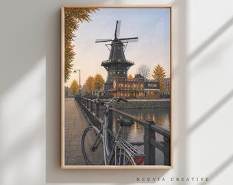 May include: A framed print of a Dutch windmill scene. A bicycle rests on a bridge overlooking a canal. The windmill is dark with a light-colored building attached. The sky is a mix of blue and orange. The print is in a light-colored wooden frame.