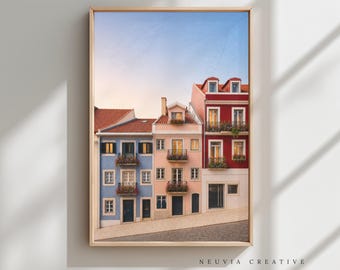 May include: A framed print featuring a row of colorful buildings with red tile roofs and balconies. The buildings are painted in shades of blue, pink, and red. The sky is a gradient of blue and orange. The print is labeled "NEUVIA CREATIVE".