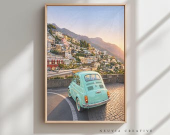 May include: A framed print featuring a vintage turquoise car parked on a cobblestone road overlooking a hillside town. The buildings are colorful, and the sky is a gradient of blue and orange. The print is labeled "NEUVIA CREATIVE".