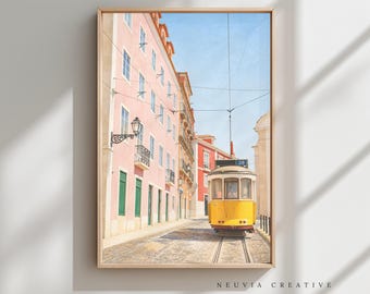 May include: Framed print of a Lisbon street scene featuring a yellow tram on tracks. The buildings are painted in shades of pink and red, with green window frames. The sky is a clear blue. The print is labeled "NEUVIA CREATIVE".