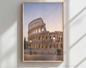 May include: Framed print of the Colosseum in Rome, Italy, at dusk. The ancient amphitheater is illuminated with warm light, set against a soft blue and orange sky. A bicycle and street lamp are in the foreground. The text "NEUVIA CREATIVE" is at the bottom.
