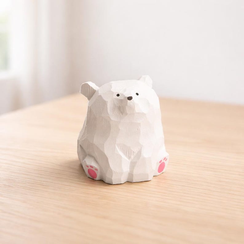 Pode incluir: Uma figura de urso polar de madeira branca esculpida com almofadas de pata rosa. O urso tem uma superf&iacute;cie texturizada e pequenos olhos e nariz pretos. A figura est&aacute; em uma superf&iacute;cie de madeira clara.