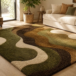 May include: A rectangular area rug with a wavy pattern in shades of green, brown, and cream. The rug is placed on a hardwood floor in a living room setting, with a sofa and plants visible in the background.