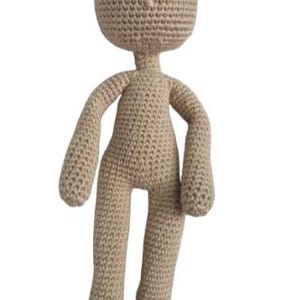May include: A handmade crochet doll in a neutral beige colour. The doll has a rounded head with small ears, black eyes, and a simple body with arms and legs. The feet are black with a grey trim. The doll is approximately 30 cm tall.