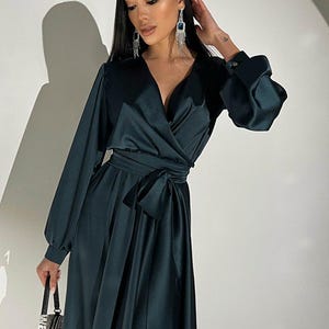 Peut inclure: Une robe portefeuille vert fonc&eacute; avec des manches longues et une ceinture assortie. La robe a un d&eacute;collet&eacute; en V et une jupe fluide. Le mod&egrave;le porte des boucles d'oreilles pendantes et un petit sac &agrave; main orn&eacute;.