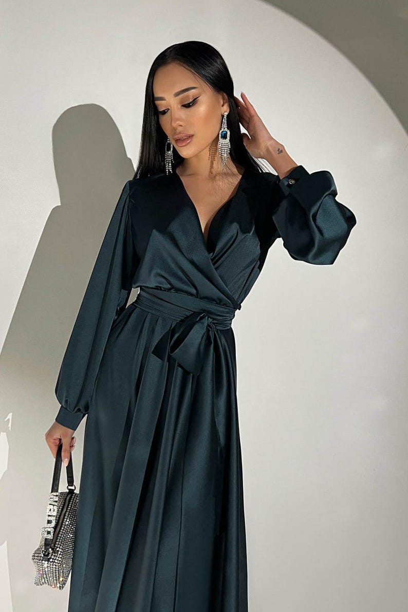 Peut inclure: Une robe portefeuille vert fonc&eacute; avec des manches longues et une ceinture assortie. La robe a un d&eacute;collet&eacute; en V et une jupe fluide. Le mod&egrave;le porte des boucles d'oreilles pendantes et un petit sac &agrave; main orn&eacute;.