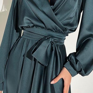 Peut inclure: Robe portefeuille en satin vert fonc&eacute; avec de longues manches volumineuses et une ceinture assortie. La robe pr&eacute;sente un d&eacute;collet&eacute; en V profond et une jupe fluide, cr&eacute;ant une silhouette &eacute;l&eacute;gante. Le tissu a un &eacute;clat subtil.