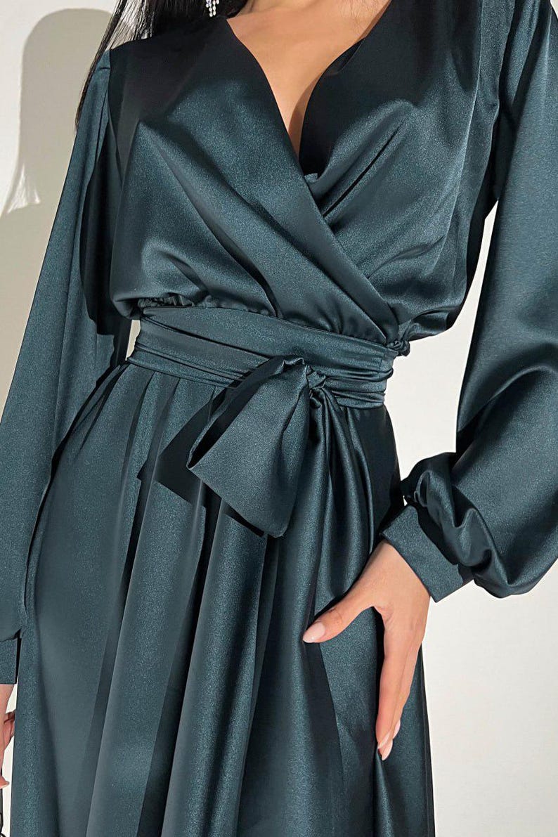 Peut inclure: Robe portefeuille en satin vert fonc&eacute; avec de longues manches volumineuses et une ceinture assortie. La robe pr&eacute;sente un d&eacute;collet&eacute; en V profond et une jupe fluide, cr&eacute;ant une silhouette &eacute;l&eacute;gante. Le tissu a un &eacute;clat subtil.