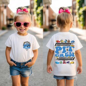 Puede incluir: Camiseta blanca con un gr&aacute;fico de coche de carreras azul y el nombre "Alex". La parte trasera de la camiseta presenta las palabras "Pit Crew" en azul, junto con varias ilustraciones de coches y un dise&ntilde;o de bandera a cuadros.