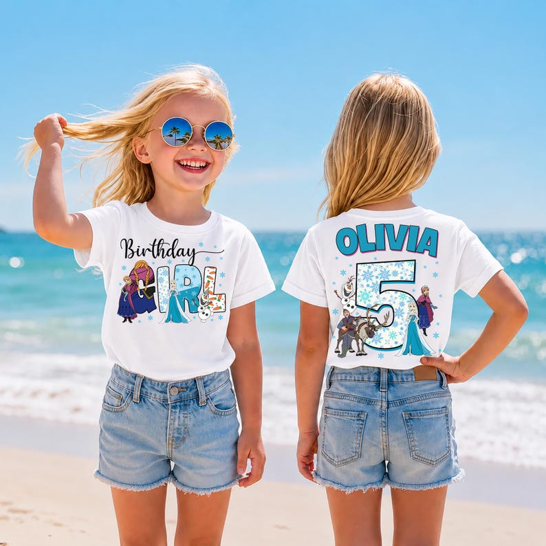 May include: Two white t-shirts with a cartoon theme. The front of the first shirt says "Birthday Girl" with cartoon characters. The back of the second shirt says "Olivia 5" with cartoon characters. Both shirts are worn by a child on a beach.