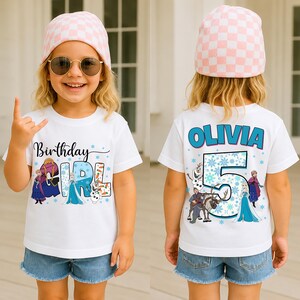 May include: A white t-shirt with a colorful graphic featuring characters from a popular animated movie. The front of the shirt says "Birthday Girl" and the back says "Olivia 5". The girl is wearing a pink and white checkered beanie and denim shorts.