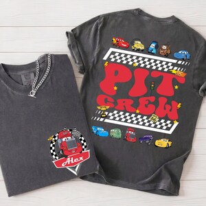 Puede incluir: Dos camisetas gris carb&oacute;n. Una presenta un gr&aacute;fico de coche de carreras con el nombre "Alex" y una bandera a cuadros. La otra tiene "Pit Crew" en letras rojas con ilustraciones de coches de carreras y un dise&ntilde;o de bandera a cuadros.