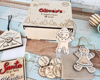 Könnte beinhalten: Ein hölzernes Weihnachts-Box-Set mit dem Text "Oliver's Christmas Magic". Enthält Lebkuchen-Ornamente, ein Santa-Schild und runde Token mit festlichen Phrasen. Das Set befindet sich auf einer hellblau-weißen Holzoberfläche.
