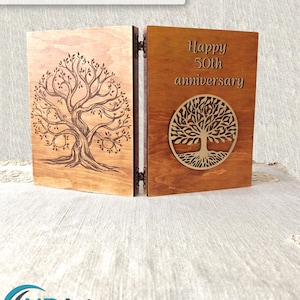 May include: A hinged wooden display board featuring a laser-engraved tree on the left panel and the text "Happy 50th anniversary" above a circular tree cutout on the right panel. The text "Laser Tested by NDARTDesignStudio" appears above.