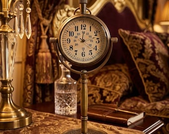 May include: A vintage-style brass clock with a round face, featuring Roman numerals and a second dial. The clock is mounted on a stand and sits on a table with a patterned runner. The clock measures approximately 6 inches in height.