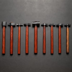 May include: A collection of eight hammers with dark wooden handles and black metal heads. The hammers are arranged in a row against a dark gray background, showcasing their different shapes and sizes, suitable for various tasks.