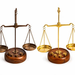 May include: Two antique balance scales. One is bronze, the other is gold. Each scale has a wooden base with weights, a central support, a horizontal arm, and two hanging pans. The scales are set against a white background.