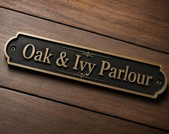 May include: A rectangular black sign with rounded corners and a gold-colored border. The text Oak & Ivy Parlour is embossed in gold lettering across the center, featuring decorative flourishes above and below the ampersand symbol.