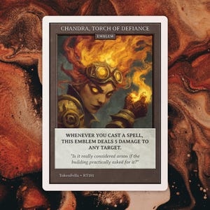 May include: A trading card featuring Chandra, Torch of Defiance. The card has a portrait of a woman with fiery red hair and goggles, holding a flame. Text on the card reads, "Whenever you cast a spell, this emblem deals 5 damage to any target."