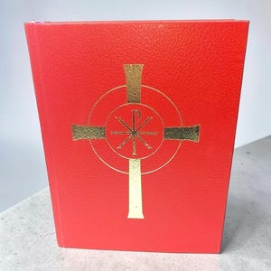 May include: A bright red hardcover book with a textured finish. Centered on the front cover is a gold foil embossed design featuring a cross enclosed within a circle, with the Chi-Rho symbol positioned in the center of the cross intersection.
