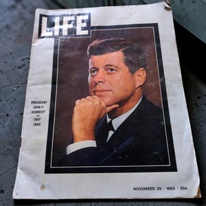 Pode incluir: Capa de revista LIFE vintage com um retrato do presidente John F. Kennedy. A capa apresenta o logotipo LIFE em branco, a data de 29 de novembro de 1963 e o preço de 25¢. A revista está envelhecida e desgastada.