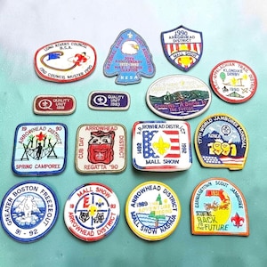 May include: A collection of fifteen embroidered scout patches in various shapes and colors, featuring text such as Long Rivers Council, Arrowhead District, 17th World Jamboree, and various dates from 1983 to 1993, displaying logos and illustrations.