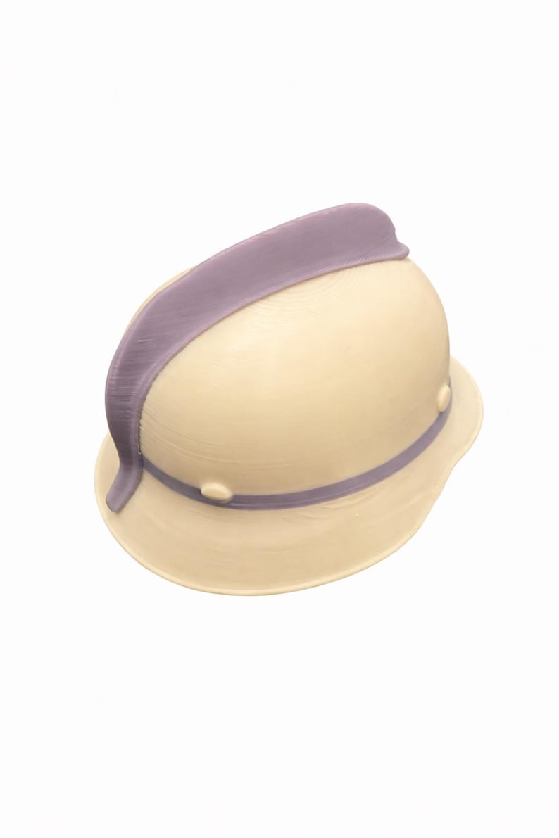 May include: A cream-colored pith helmet with a lavender band and trim. The hat has a rounded crown and a wide brim, with two small, round rivets on the side. The lavender band wraps around the base of the crown.